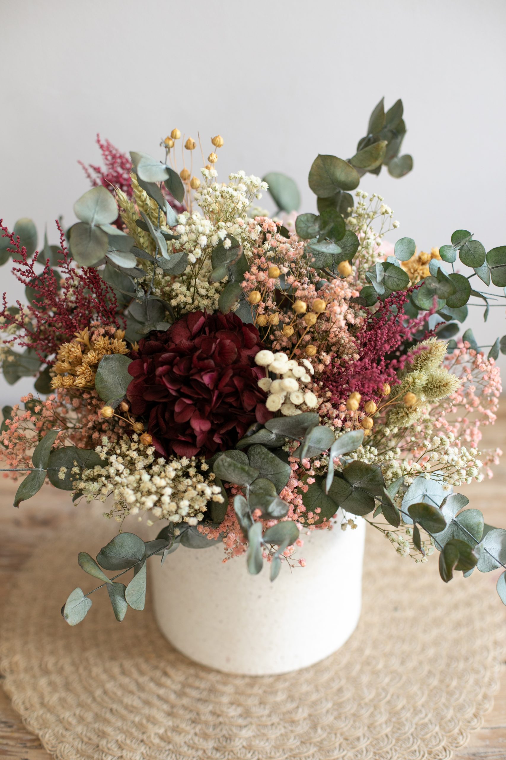 Jarrón de cerámica con flores preservadas en tonos rosa y granate